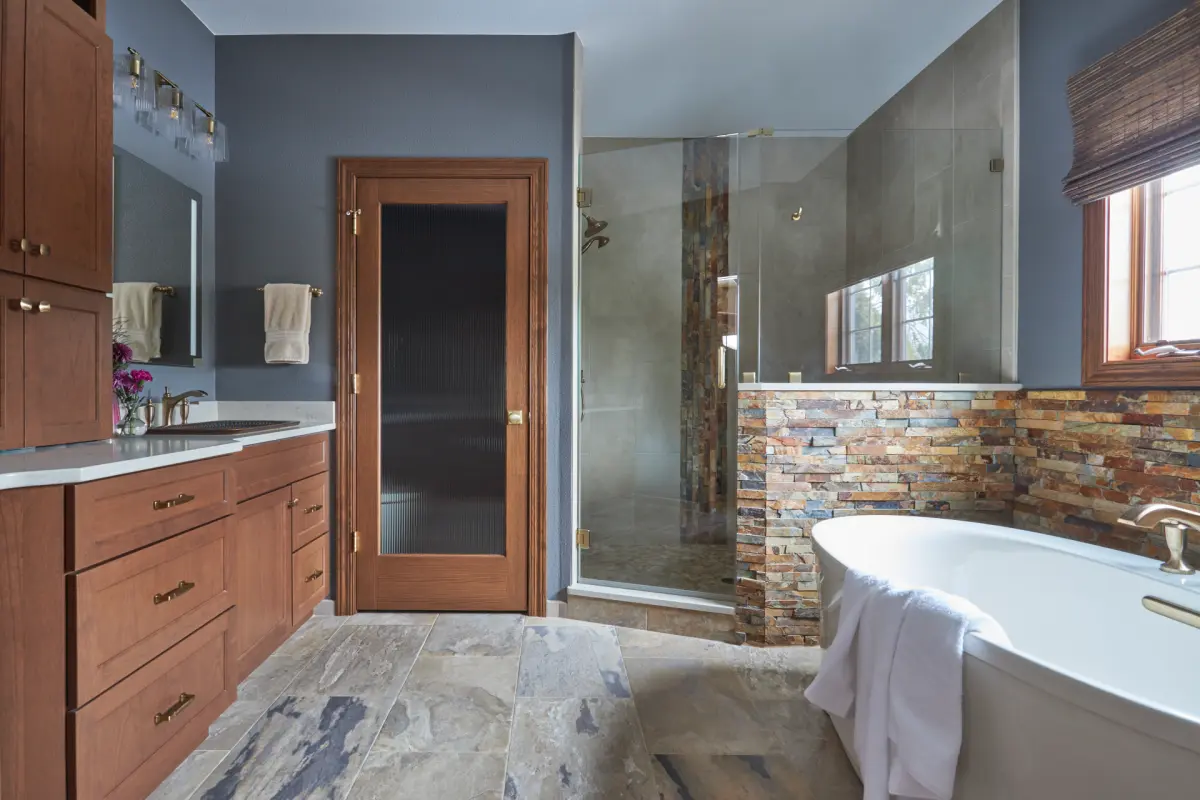 Grafton-Primary-Bath-1-rszd-scaled Grafton bathroom with wood vanity cabinetry, blue-gray walls, a glass shower, and a freestanding tub.
